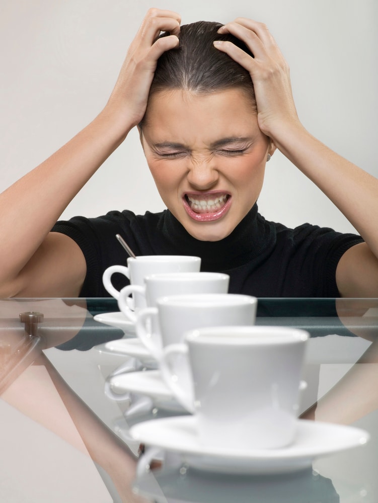 Woman with Headache sitting with four cups of coffee